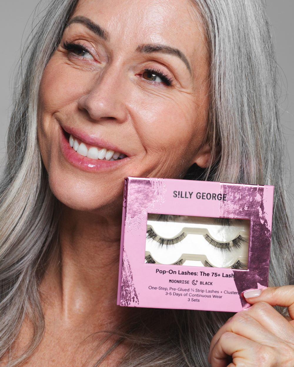 Woman holding a pink package of black Moonrise Pop-On Lashes: The 75+ Lash 